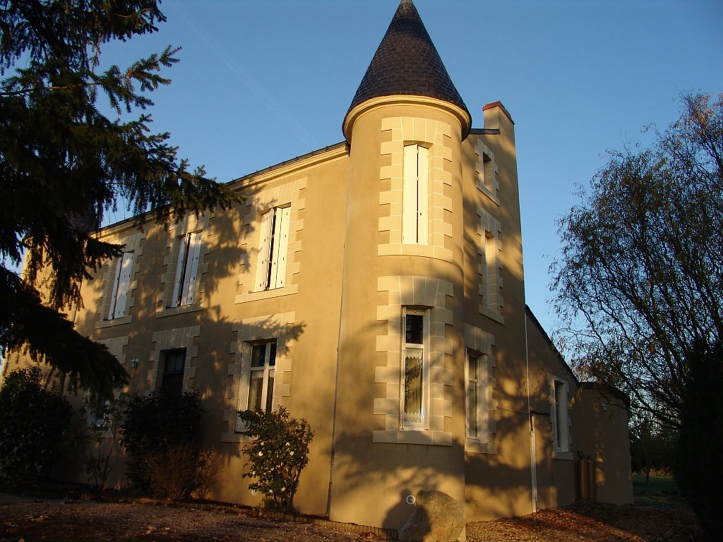 Manoir à tourelle en pierre claire et fenêtres blanches au soleil couchant.