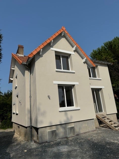 Maison deux étages, façade beige, toit tuiles orange et fenêtres blanches.