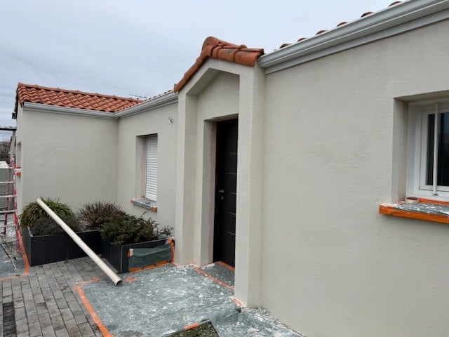 Façade rénovée avec enduit crème, porte d'entrée noire et toit en tuiles terre cuite.