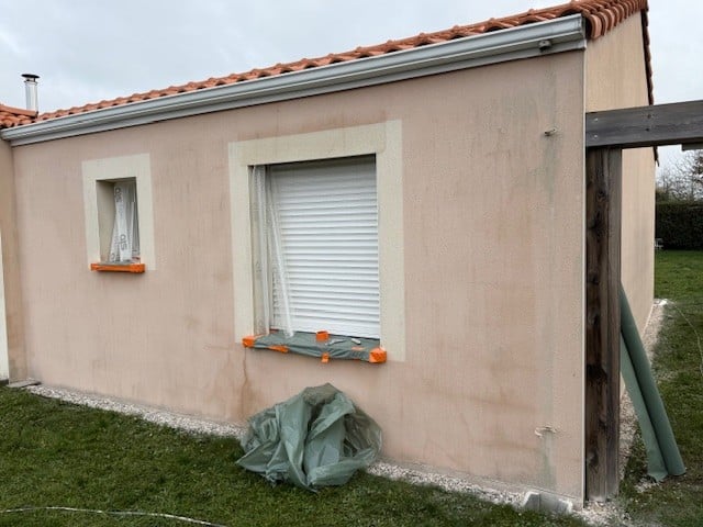 Mur extérieur beige en rénovation, fenêtres à volets blancs et bâches de chantier.